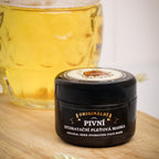 Black jar of 'Pivni' beer facial mask on a wooden surface with a glass of beer in the background.