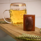 Glass of beer on a wooden surface with a small wooden barrel-shaped object and wheat stalks.