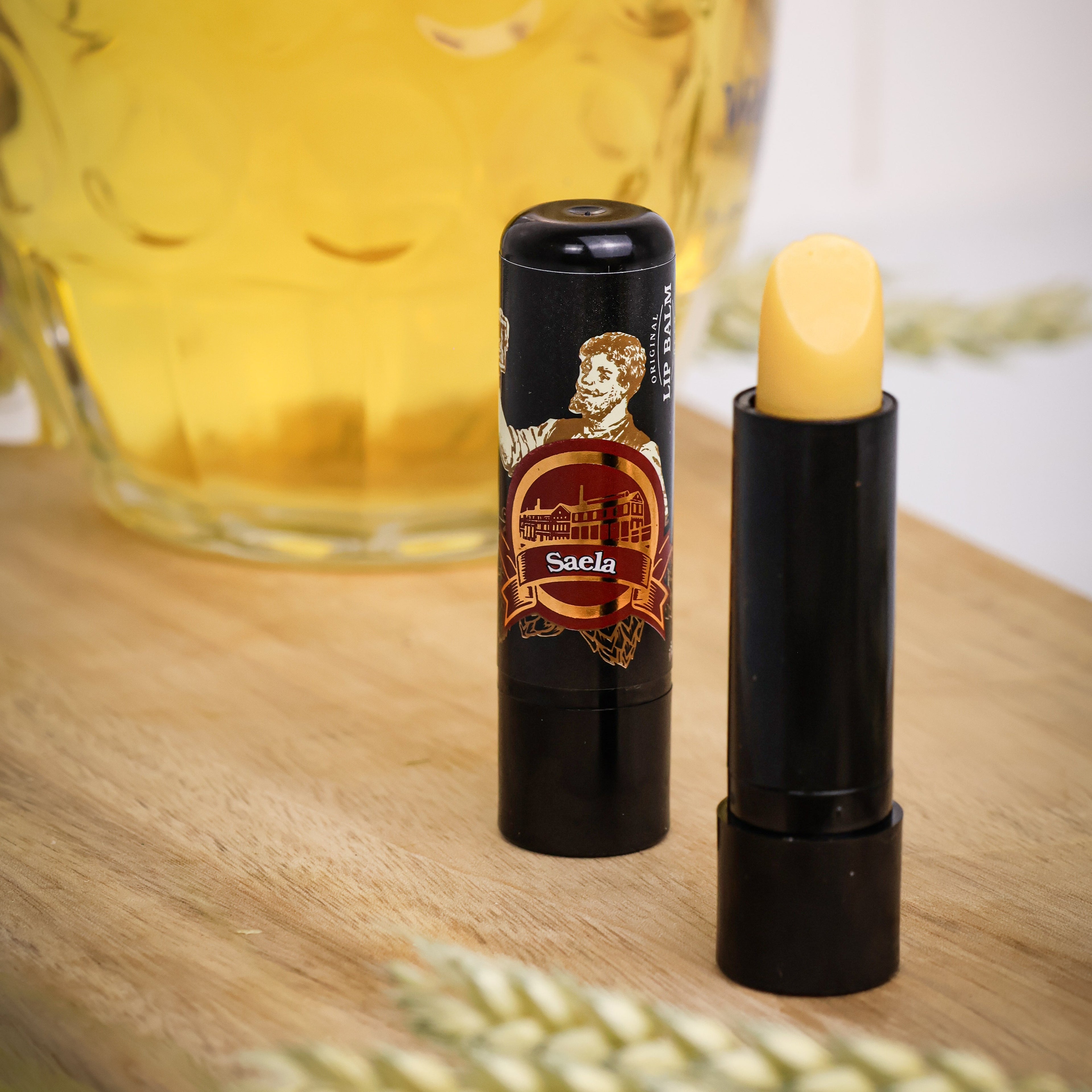 Lipstick with a decorative case on a wooden surface next to a glass of beer.