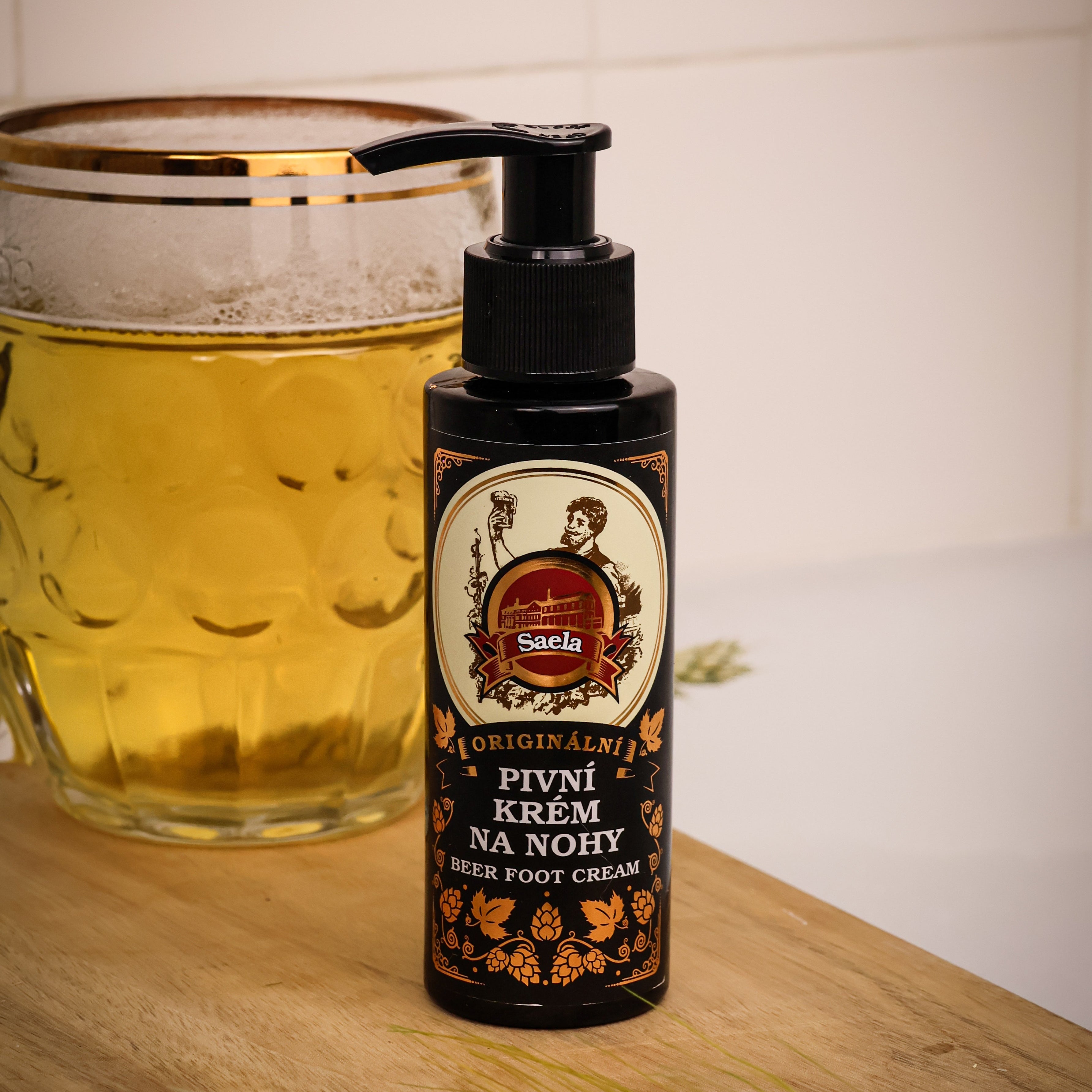 Bottle of foot cream with a label next to a glass of beer on a wooden surface.