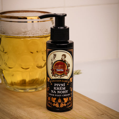 Bottle of foot cream with a label next to a glass of beer on a wooden surface.